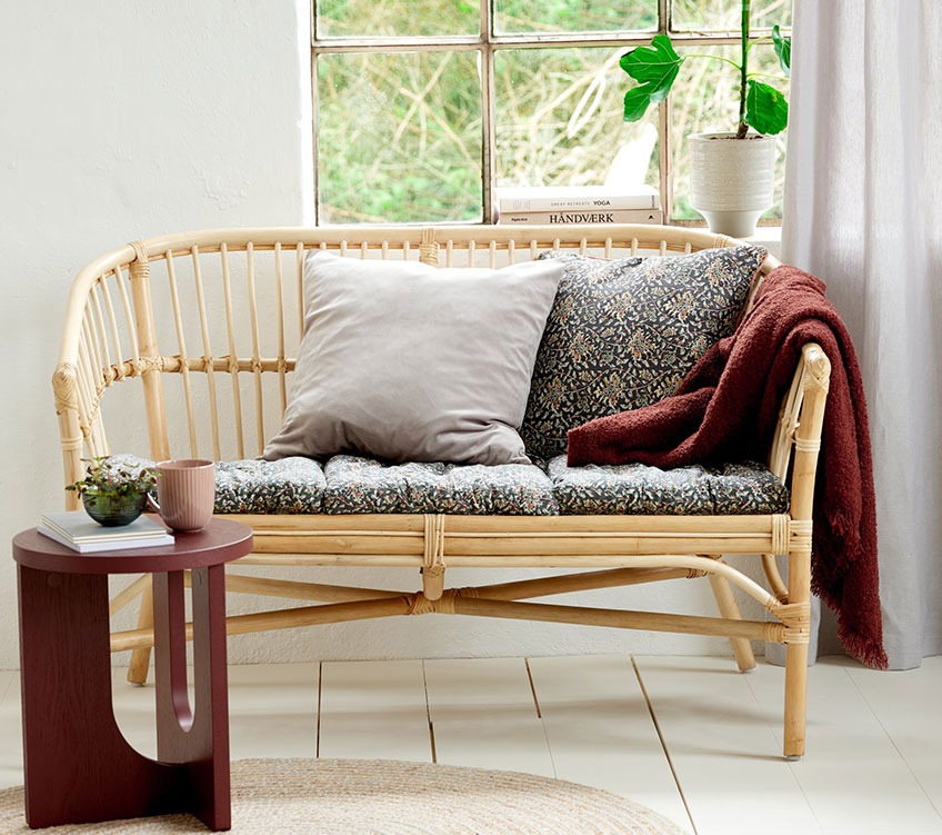 2-seater sofa in rattan with seat pads and back cushions, burgundy throw and a round end table 