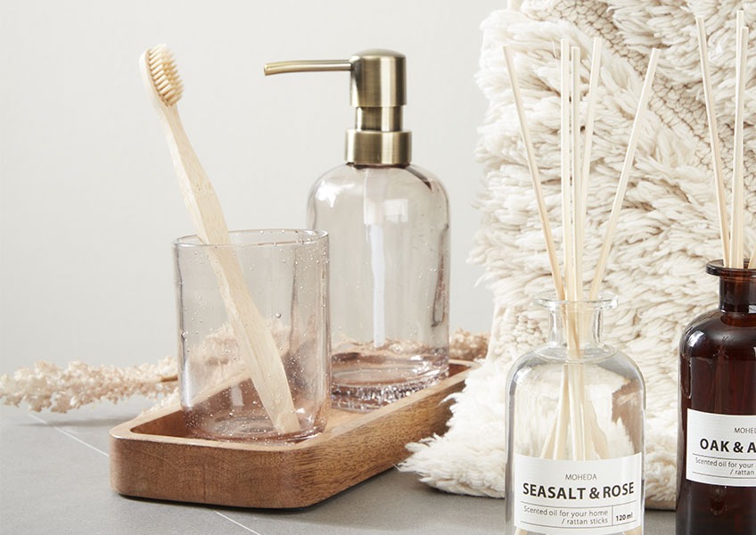 Soap dispenser and toothbrush holder made from recycled glass placed on wooden tray