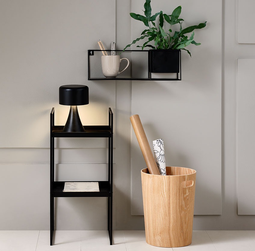Wooden basket on the floor below a black shelf with a plant pot 