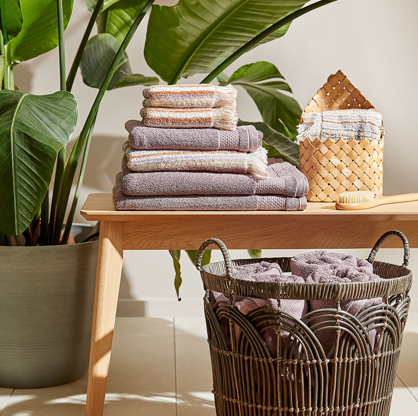 Cotton towels and a wicker basket on a bench in a bathroom 