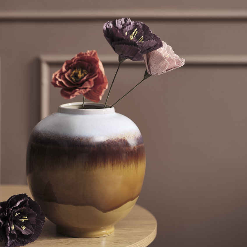 Multicoloured vase on table with artificial flowers in red, purple, and pink