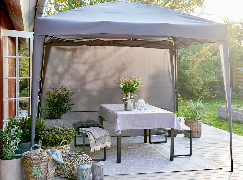 Grey gazebo with a decorated and set table and benches on patio 