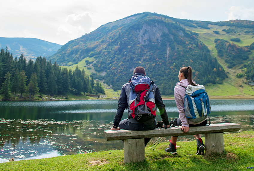 Man and woman sitting on bench overlooking mountain lake